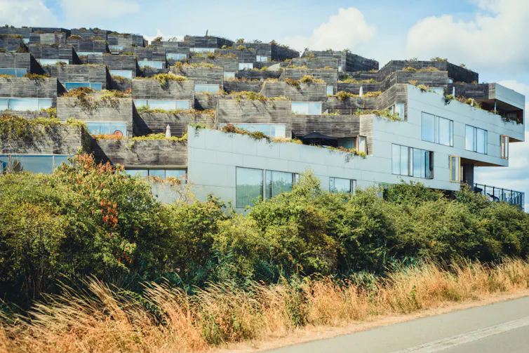 Rows of white and grey houses on a grassy rise next to a road