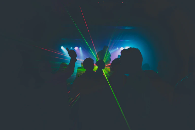 Laser lights against silhouettes of people dancing in a dark night club.