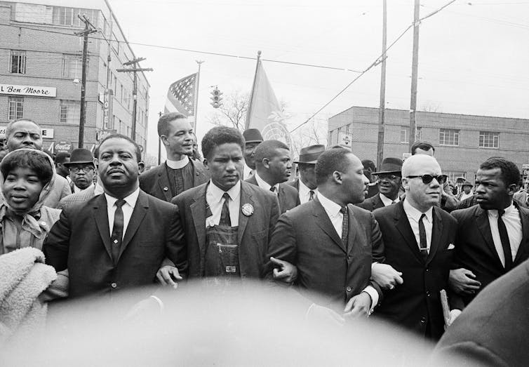 News photo: men in suits marching.