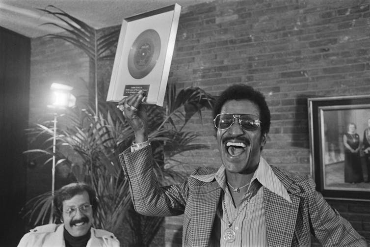 Davis holds a framed record above his head.