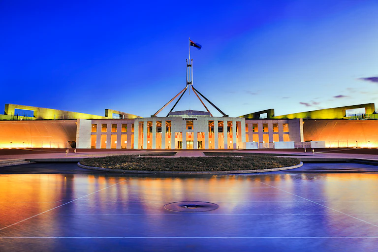 The front of Parliament House in Canberra set against an evening sky.