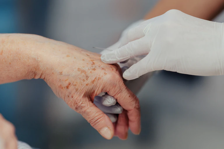 Gros plan sur la main d'une soignante infirmière qui administre des médicaments par voie intraveineuse à une dame âgée.