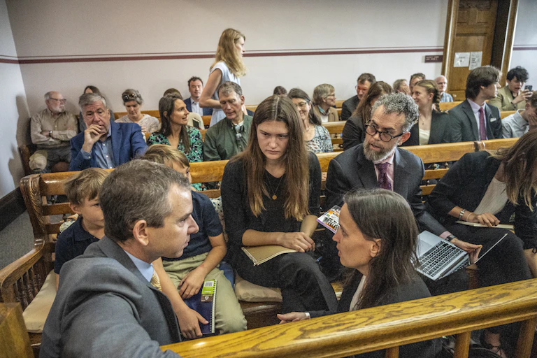 A group of young people confer with older people wearing suits in a courtroom.