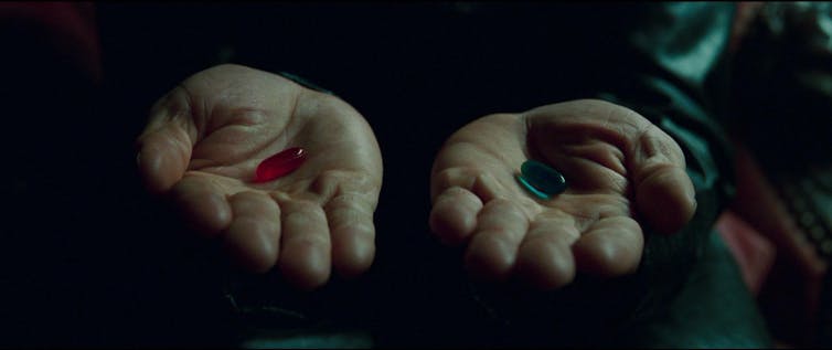 Dos manos sostienen una pastilla roja y otra azul.