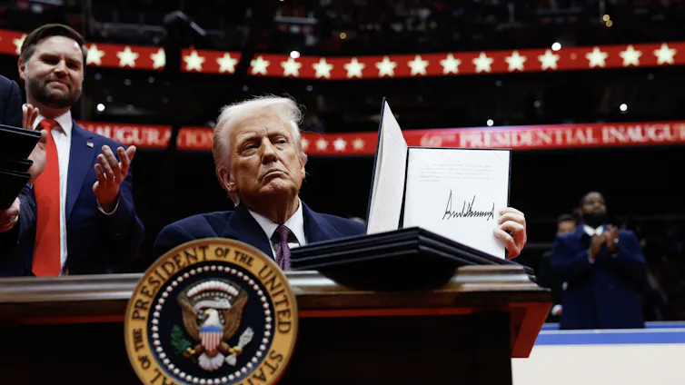 Donald Trump holds up a signed executive order while J D Vance looks on.