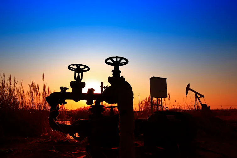 A valve and an oil derrick at dusk.