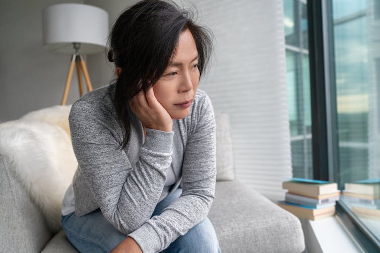 An woman on a white sofa looking out a window with her chin in her hand