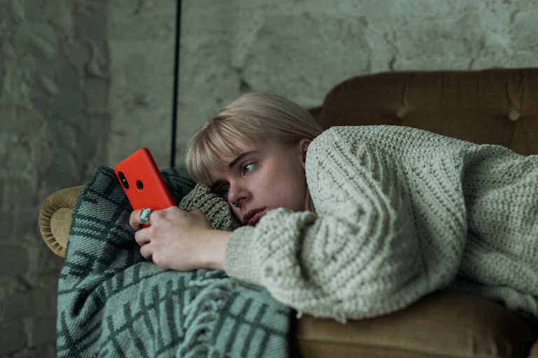 Young woman lying on sofa and scrolling through her smartphone