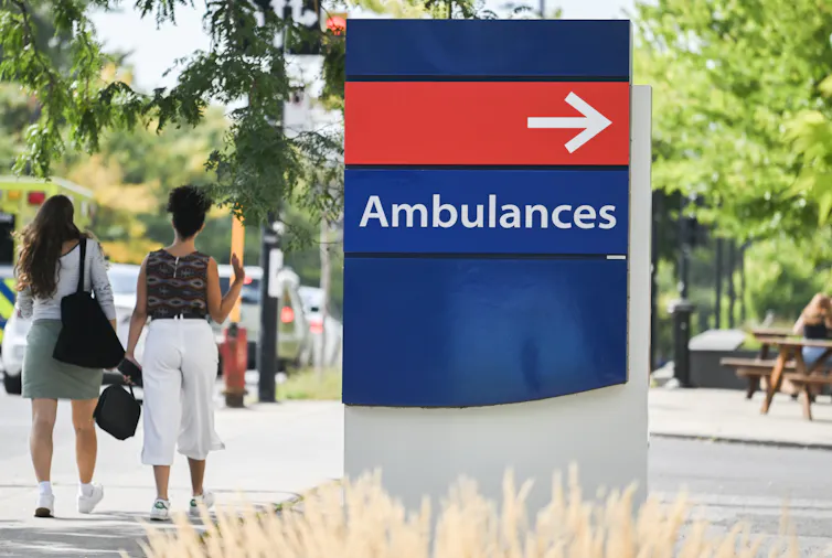 People walk past an ambulance sign at a hospital