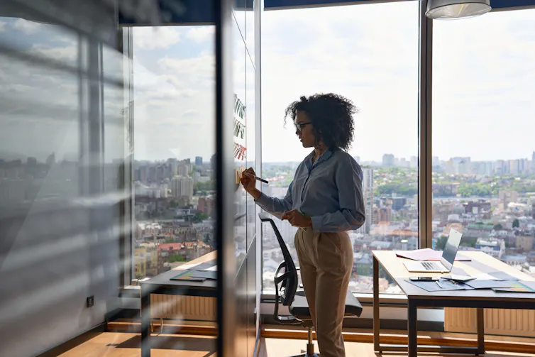 A young woman writes on a whiteboard in an office