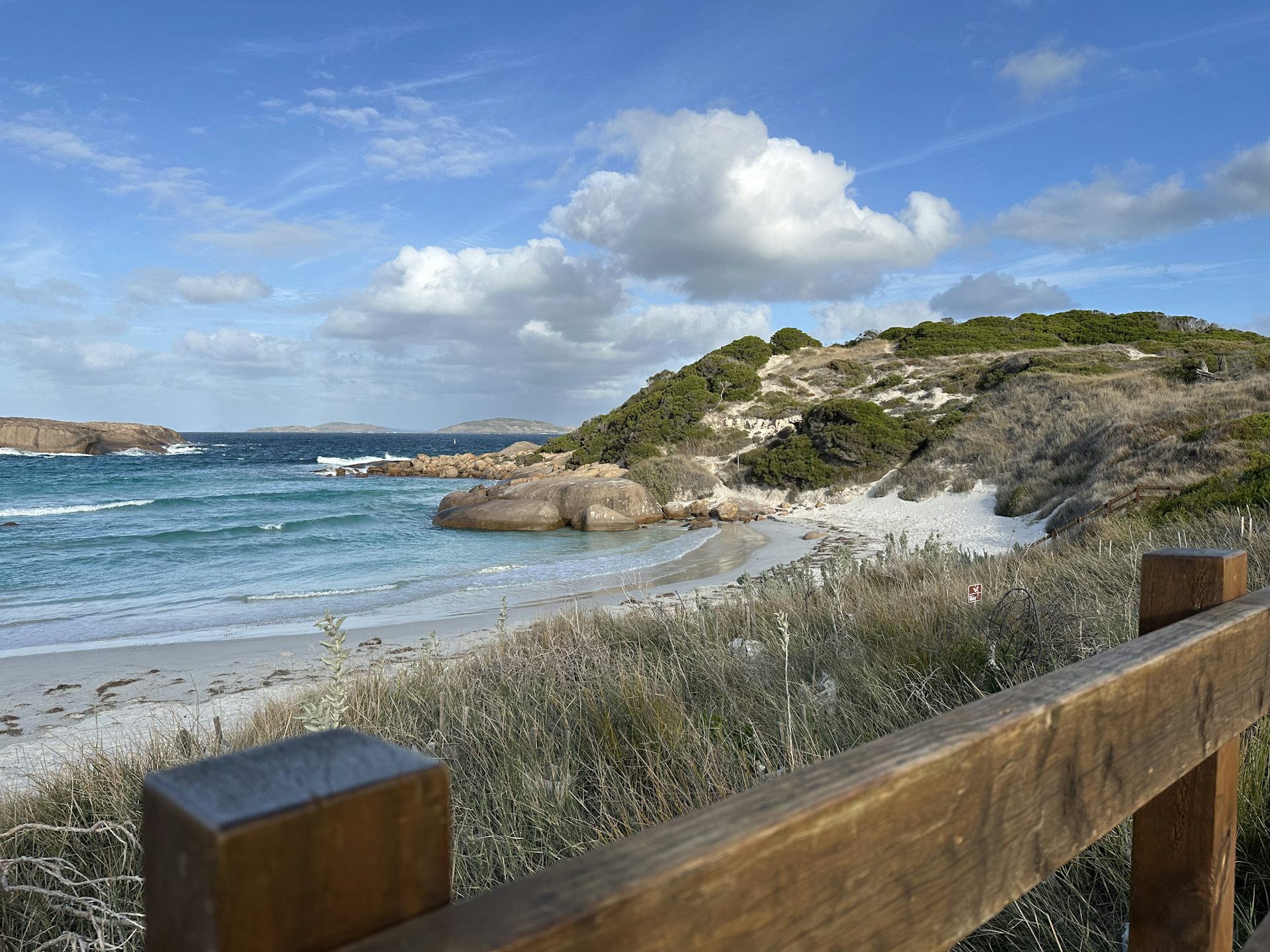 A beach scene with a fence in the foreground to provide visual depth.