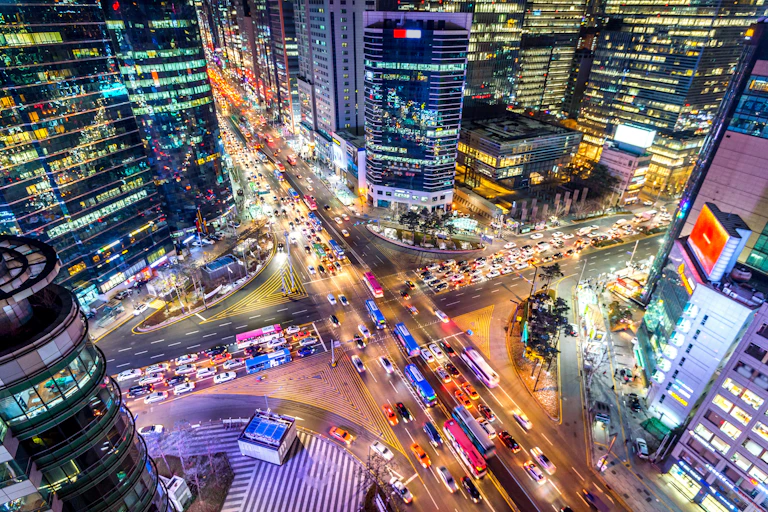 Nighttime aerial view of a busy colourful intersection in Seoul, with vivid colours and a sense of bustling life.