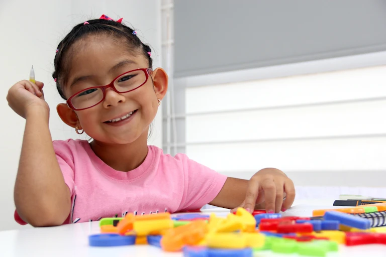 Four year old girl wearing glasses at desk with puzzles pieces or letters