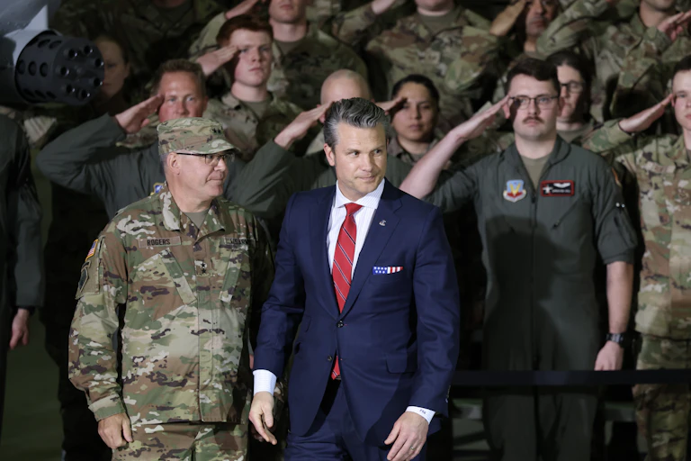 Defense Secretary Pete Hegseth with US troops saluting in background