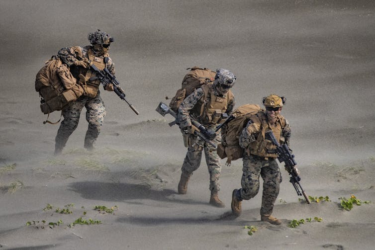 Three US Marines carrying equipment and weapons in the open.