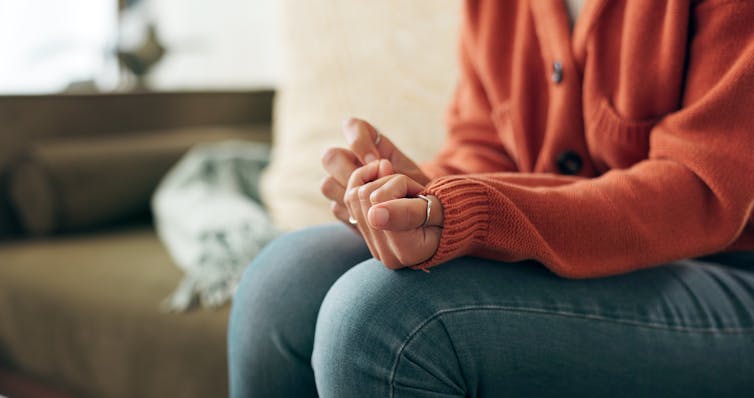 A woman sitting on a couch curls her hands into a fist.