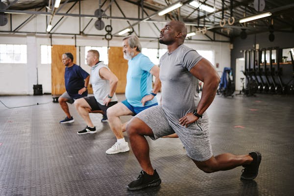 A group of men perform a lunge together in a gym.