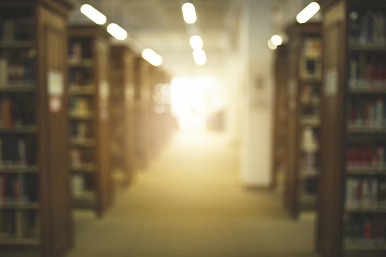 Light appears at the end of a library hallway lined with bookshleves.