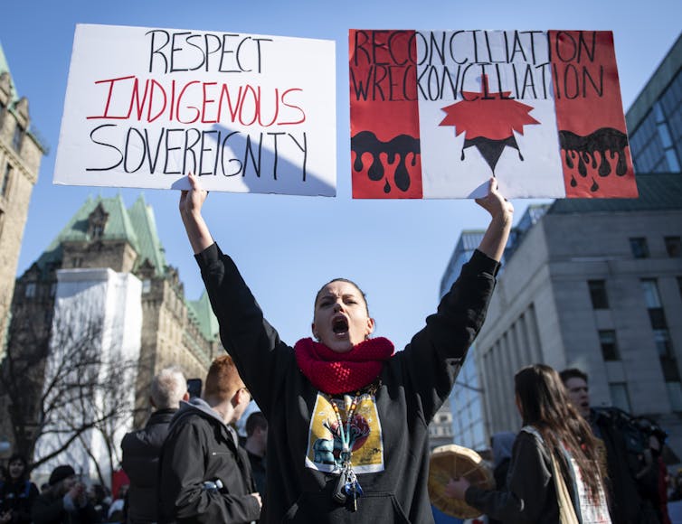 A woman holds up a sign at a protest that reads Respect Indigenous Sovereignty