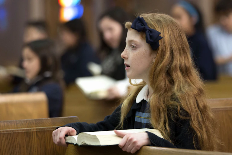 A young girl with red hair holds a bible.