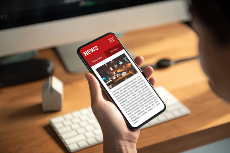 A person holding a smartphone displaying a news app