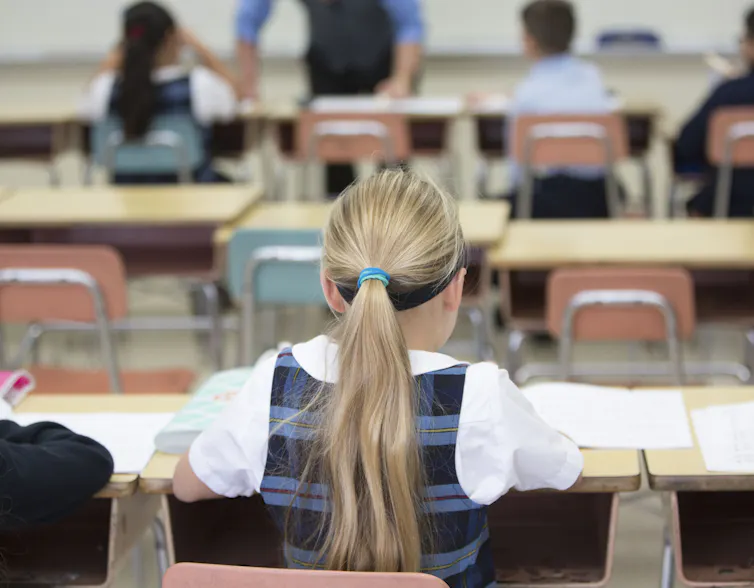 A rear view of a girl siting at her desk in class.