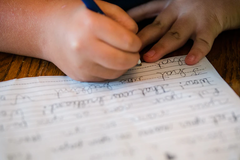 Child's hand shown writing in cursive in a notebook