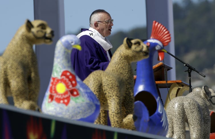 Animal figurines in front of a man in a purple robe speaking into a microphone.