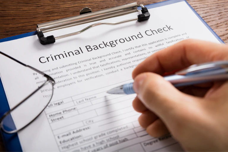 Hand completing a background check form.