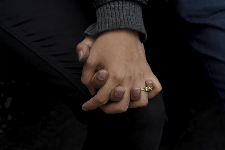 Gros plan sur deux personnes se tenant la main. Une bague en diamant est visible à un doigt