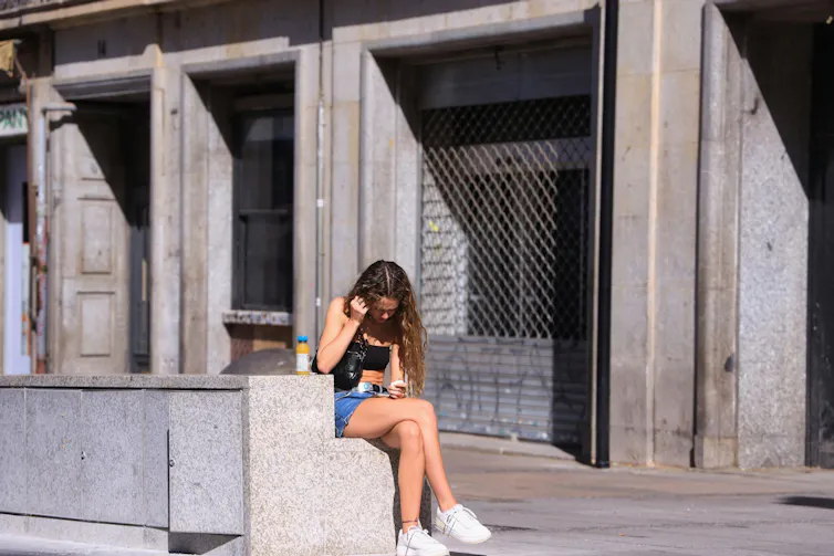 Una mujer sentada sola en un banco en la calle atiende a su teléfono móvil.