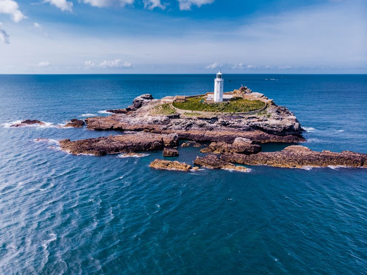white lighthouse on rocky outcrop, surrounded by sea