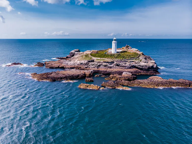white lighthouse on rocky outcrop, surrounded by sea