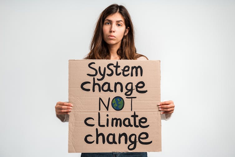 Why weather execs are frequently held to unrealistic requirements 1 woman holds cardboard protest sign, system change not climate change