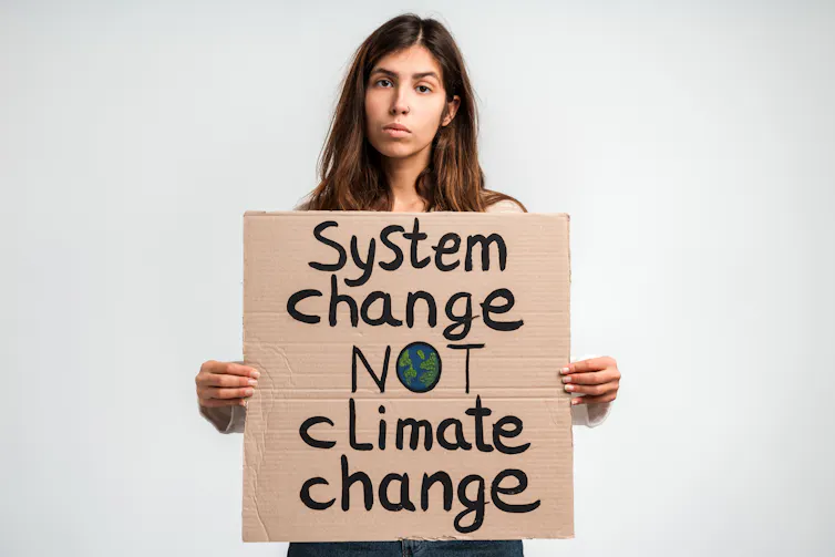 woman holds cardboard protest sign, system change not climate change