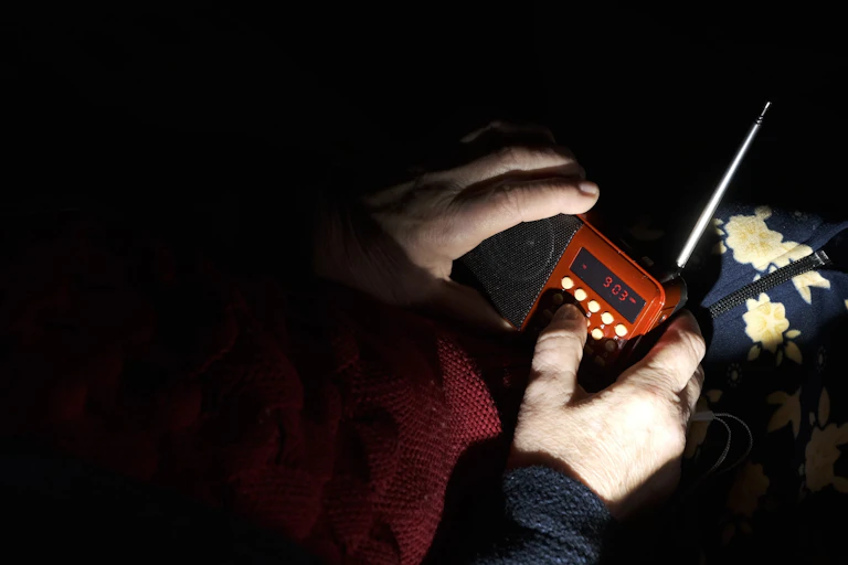 Unas manos sujetan una radio a oscuras, bajo la luz de una linterna.
