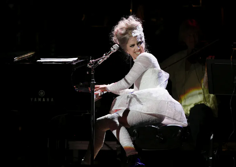 A woman plays the piano with her head turned and a toothy smile with head turned away from piano.