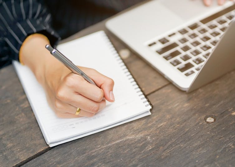 Person at a laptop writing in a pad