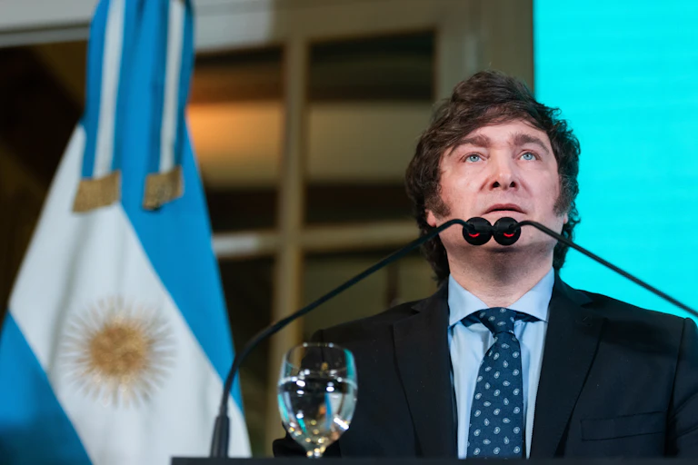 argentinian president javier milei standing in front of flags and microphones