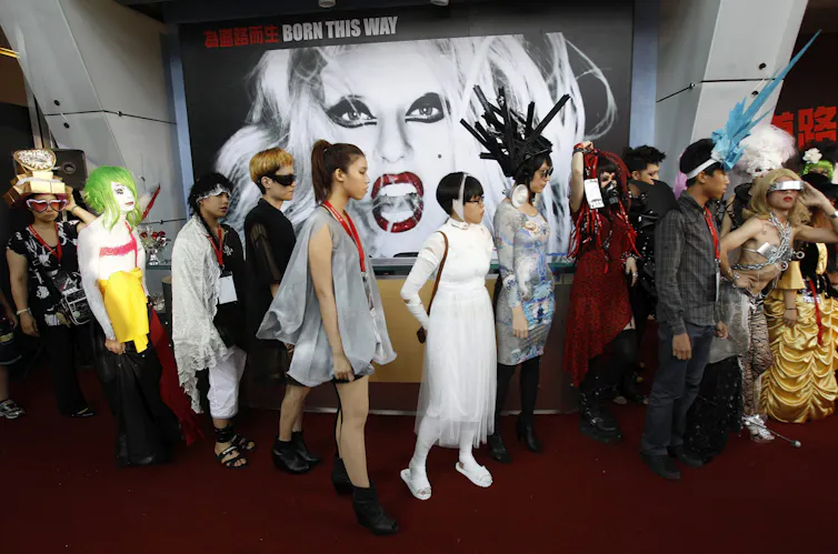 People in a line in front of a large image of a woman with blond hair and open red lips who appears to be snarling.