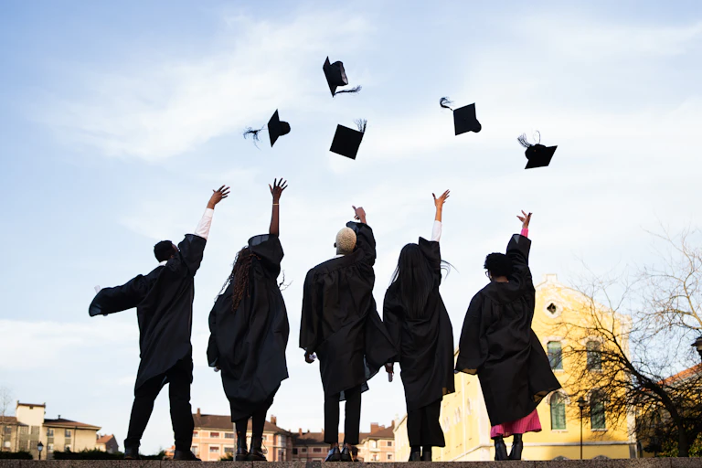 Graduates wearing black robes throwing mortarboards in the air.