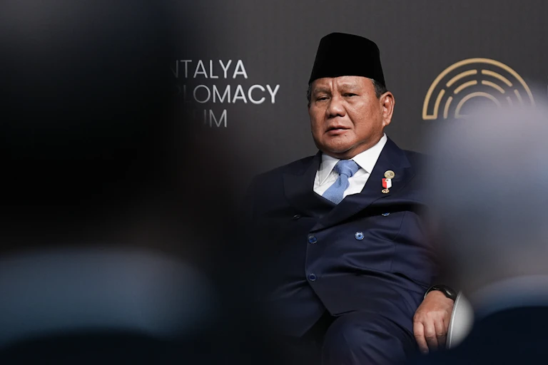 A man in a suit and a traditional Indonesian hat is seated.