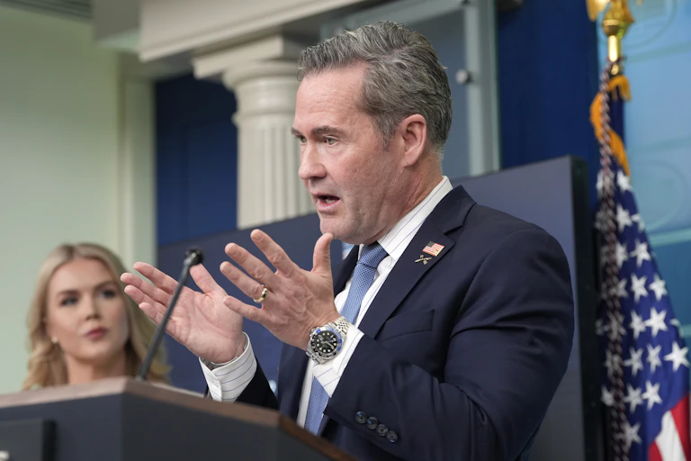 A man in a suit and tie, with hands open, speaks at a lectern.