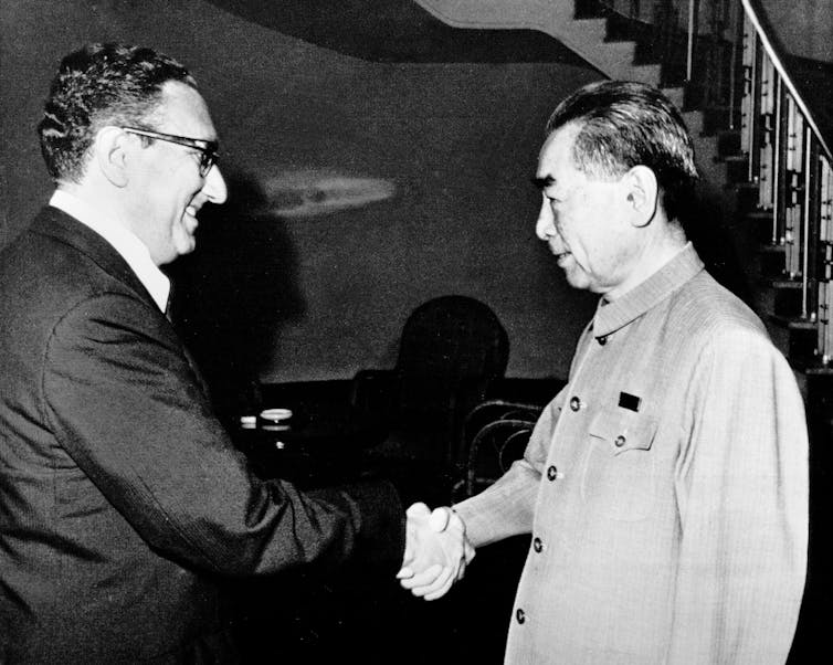A man in a dark suit shakes the hand of a man dressed in a Tang suit.