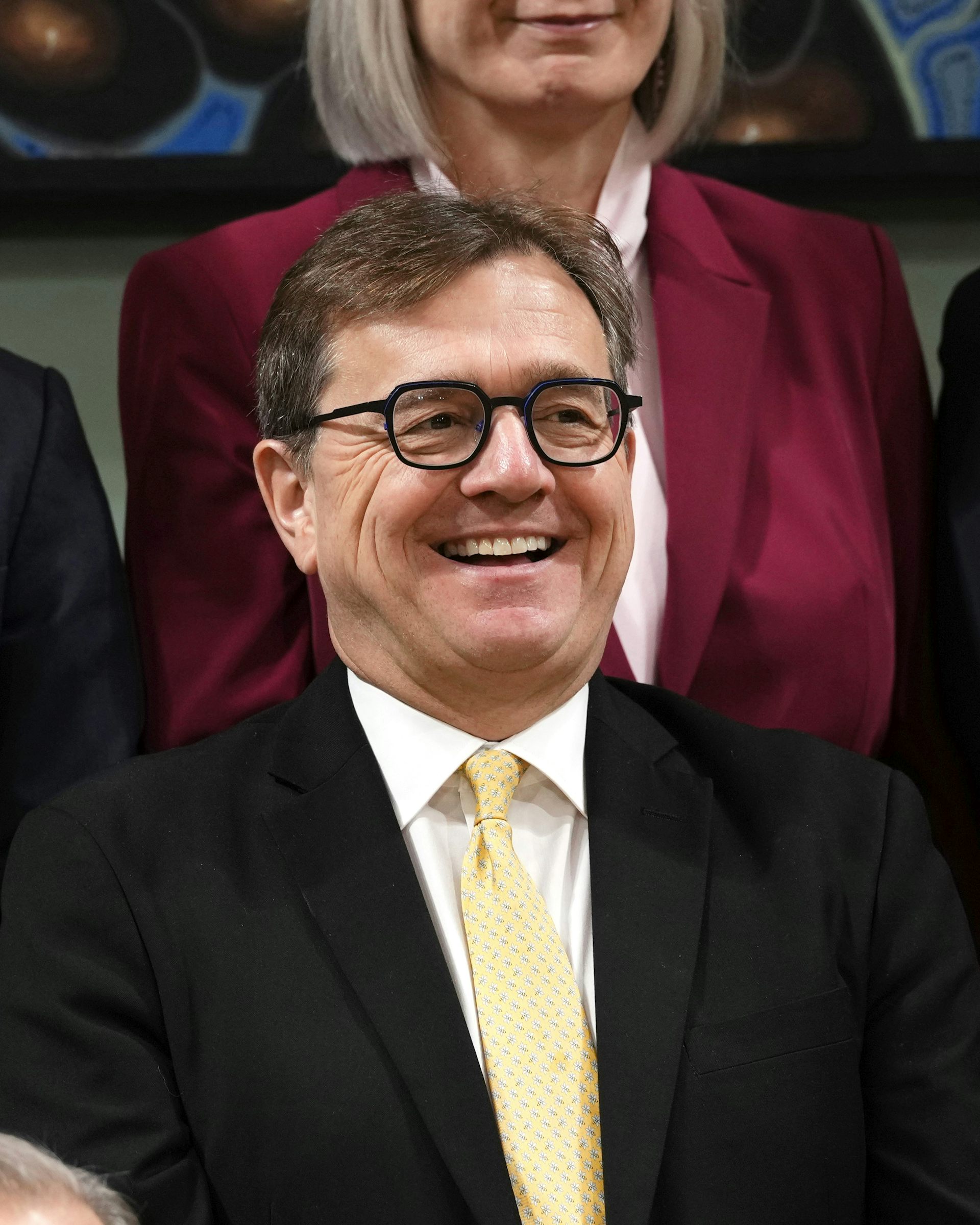 Un hombre con cabello oscuro y gafas sonríe.