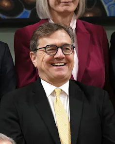 Un hombre con cabello oscuro y gafas sonríe.