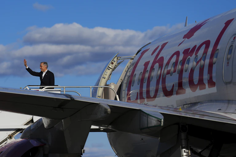 A man waves as he gets onto an aircraft with a large Liberal logo on its fuselage.