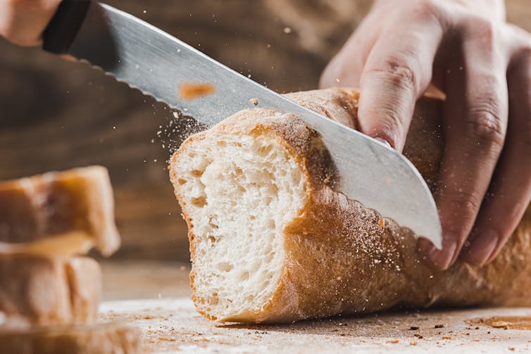 Kinfe slicing through a crusty loaf of bread.