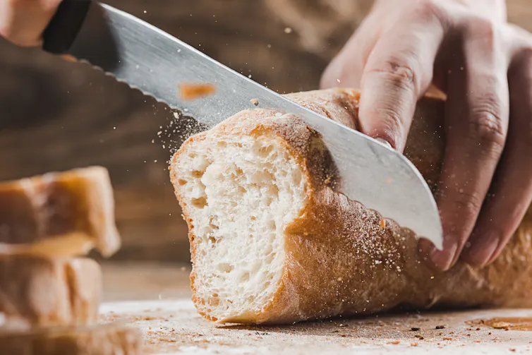 Kinfe slicing through a crusty loaf of bread.