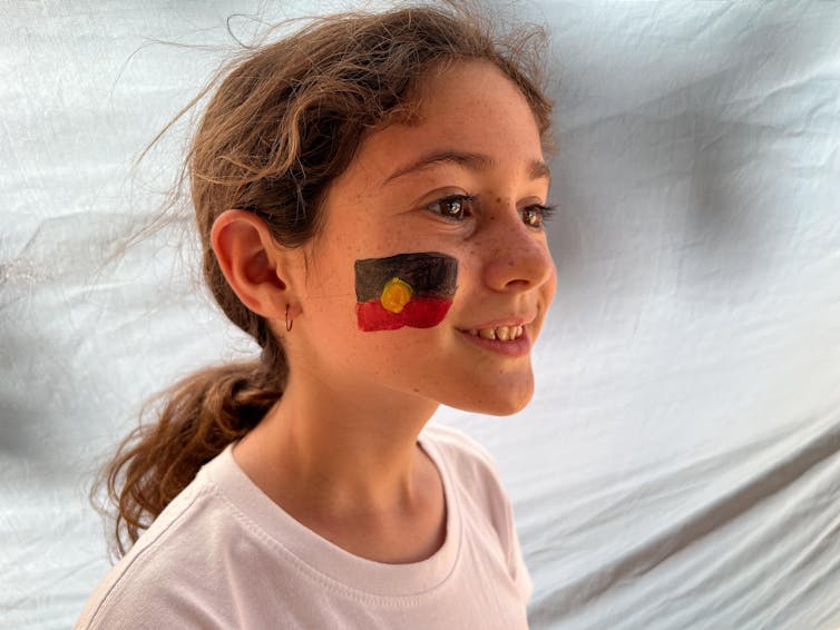 Smiling young girl in a white t-shirt with the Indigenous flag painted on her cheek.